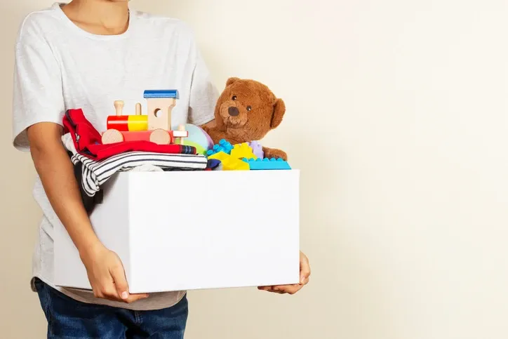 Donation concept. Kid holding a donation box with books, clothes, and toys.