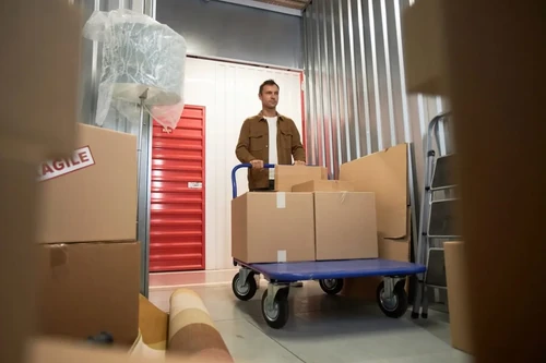 A man pushing a cart of sealed boxes into a storage unit.