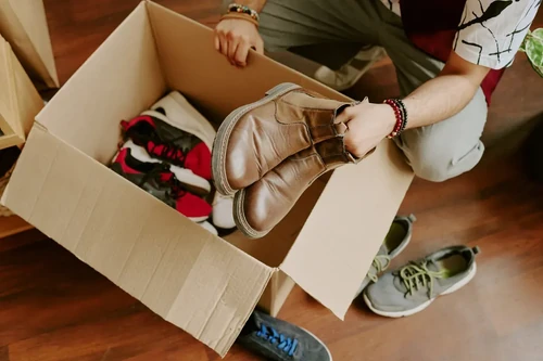 A man packs seasonal clothing and shoes into a cardboard box for storage.